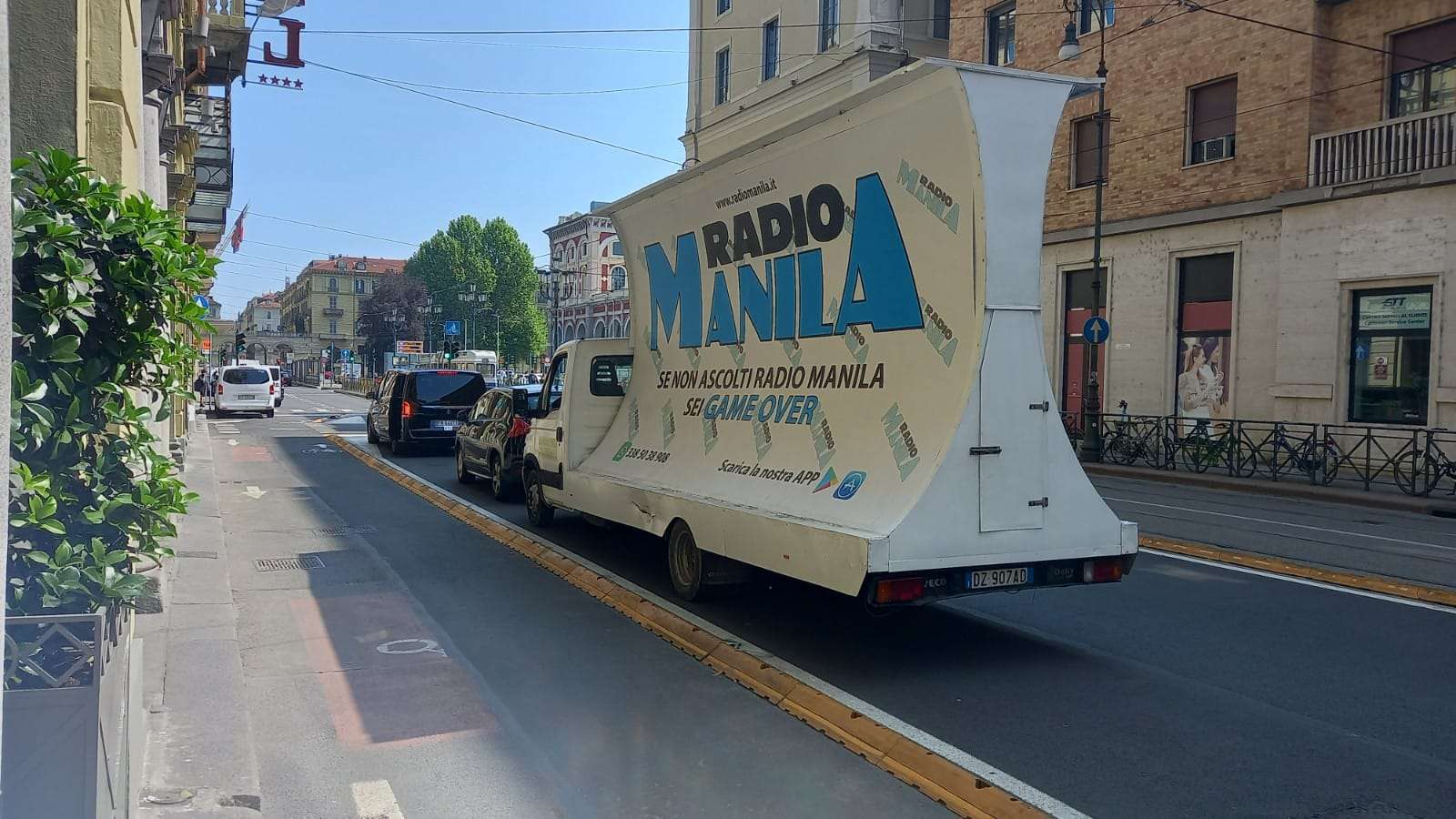 Camion vela con campagna pubblicitaria Radio Manila lungo una via di Milano