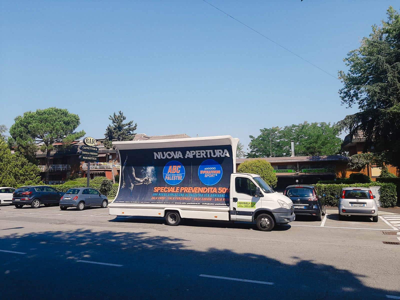 ABC Palestre Cesano Boscone (5)-175 Camion vela pubblicitario blu con campagna nuova apertura parcheggiato su una strada alberata