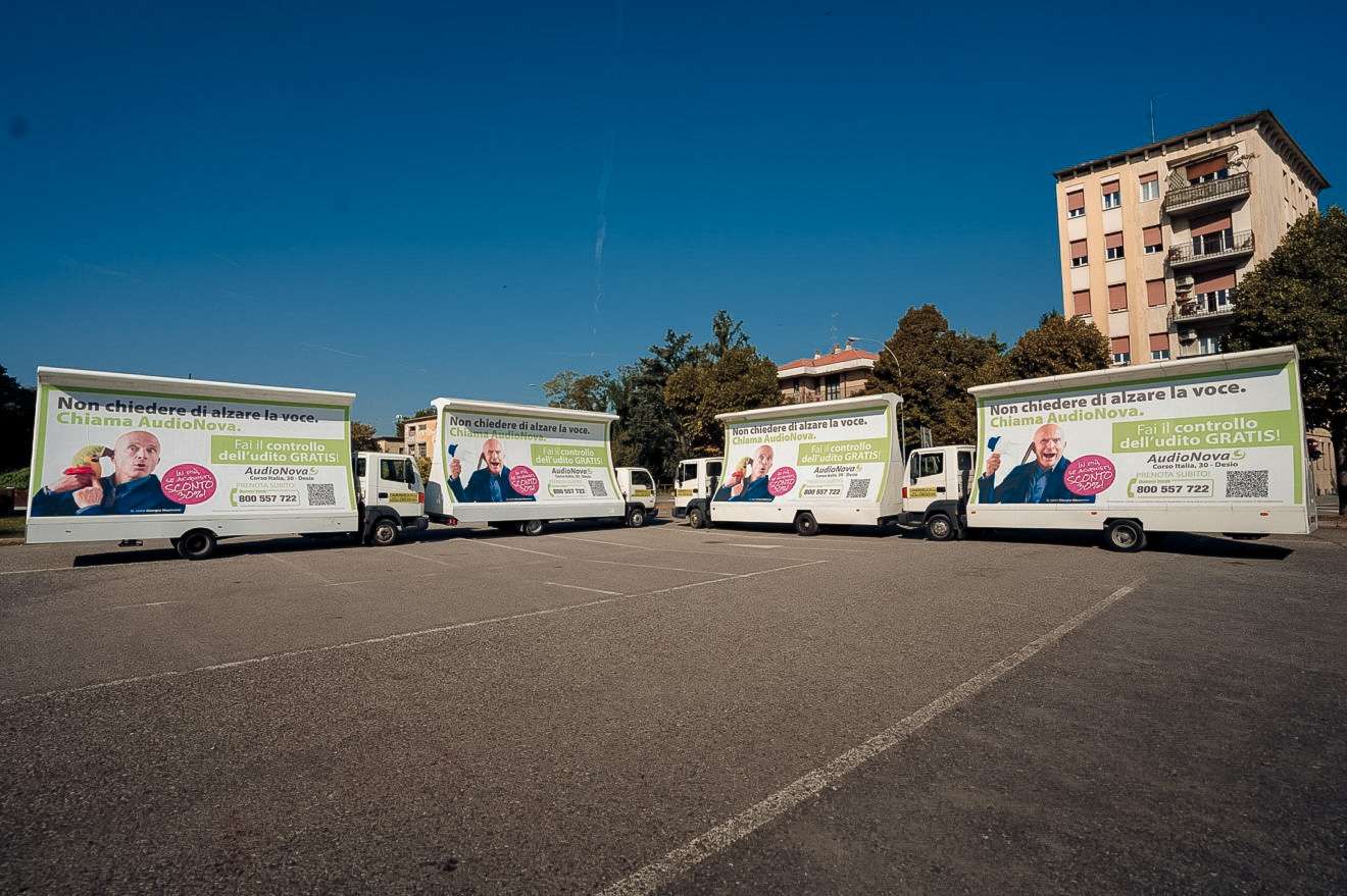 Flotta di camion vela pubblicitari Audionova allineati in un parcheggio a Desio